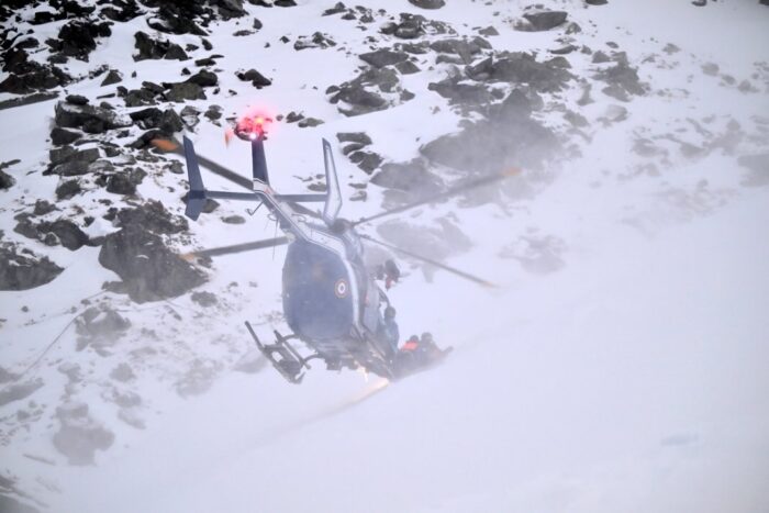 A helicopter touching ground during a mountain rescue in snowy terrain. 