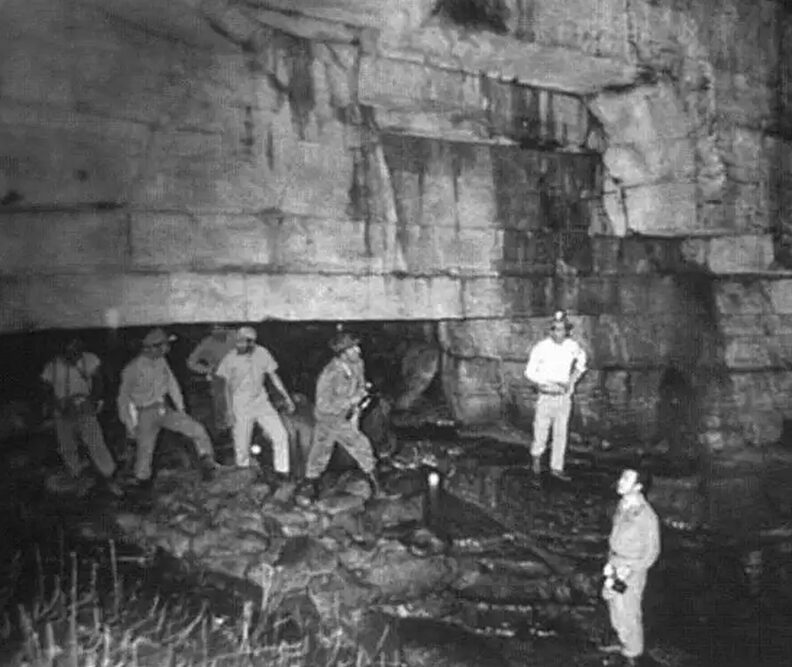 bw photo of people standing at a cave entrance
