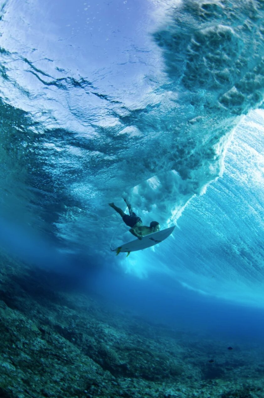 A surfer dives under the water to avoid a wave on Cloudbreak Reef in Fiji