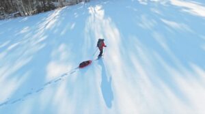 An aerial shot of Dianne Whelan pulling a sled along a snowy trail in Canada.