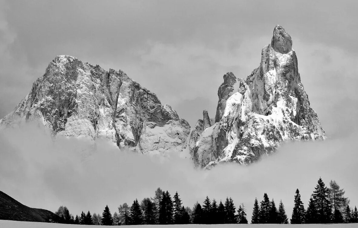 The peaks of Cimon della Pala and Cima Vezzana emerging from fog and low clouds after a snowstorm.
