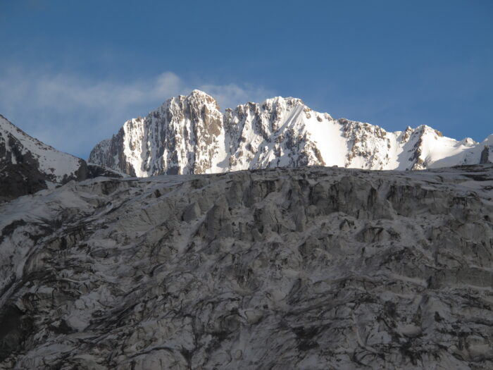 A vertical north face lit by the sun, as seen from a broken glacier. 