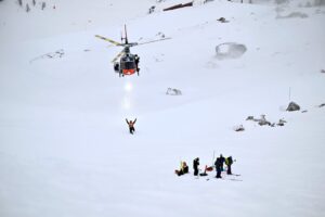 A helicopter arrives to a snow-covered area where a group of rescuers await.