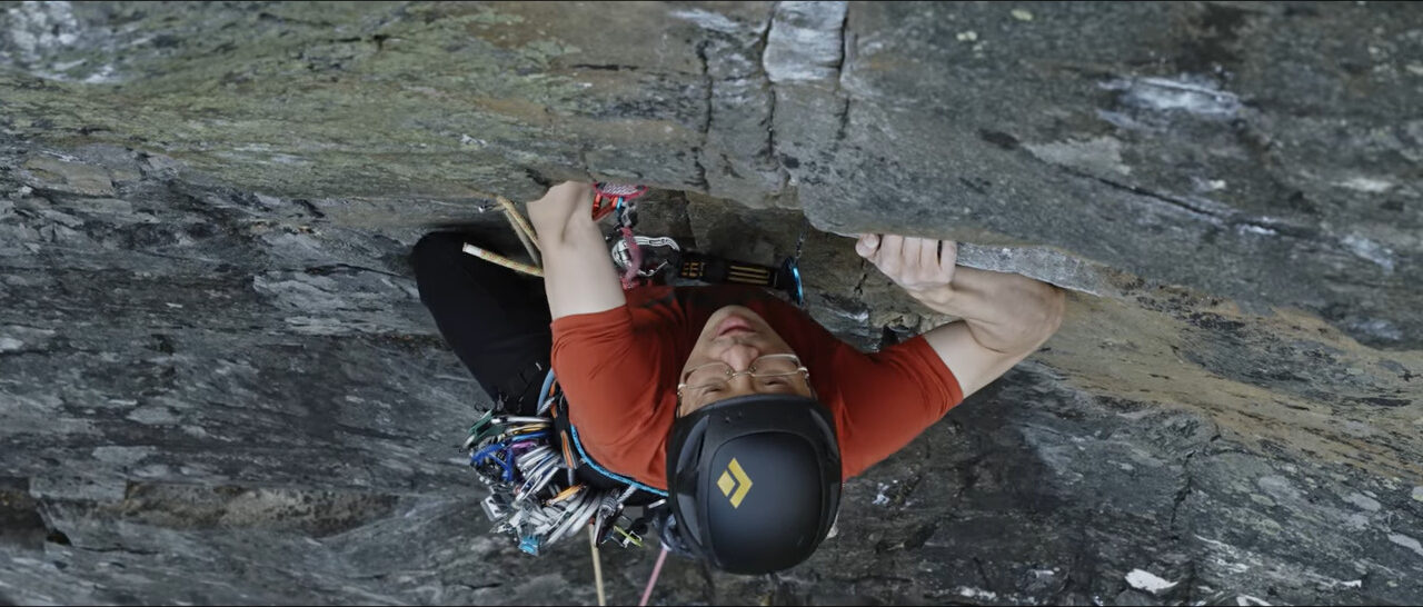 A man trad climbing on a sheer grey rock face