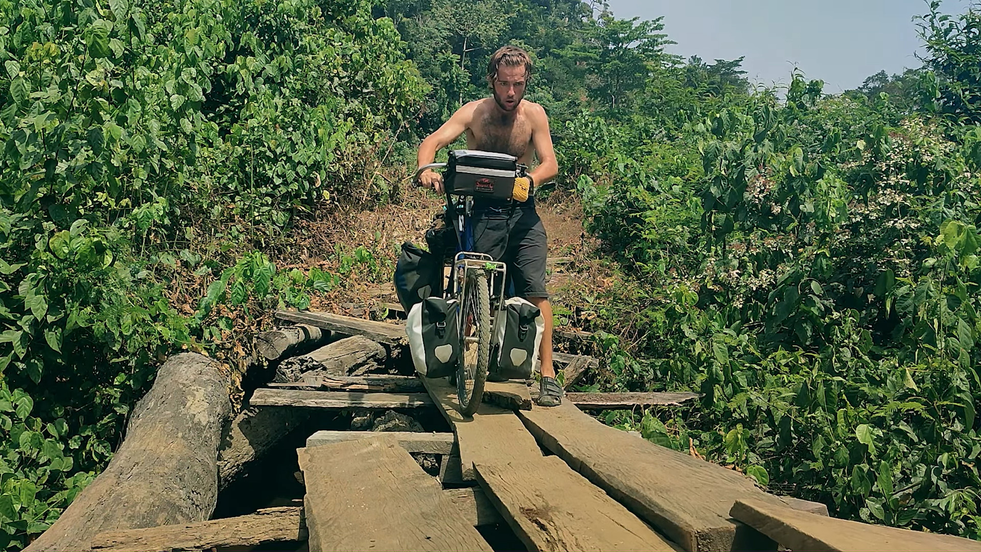 A man pushing a bike over a rickety wooden bridge
