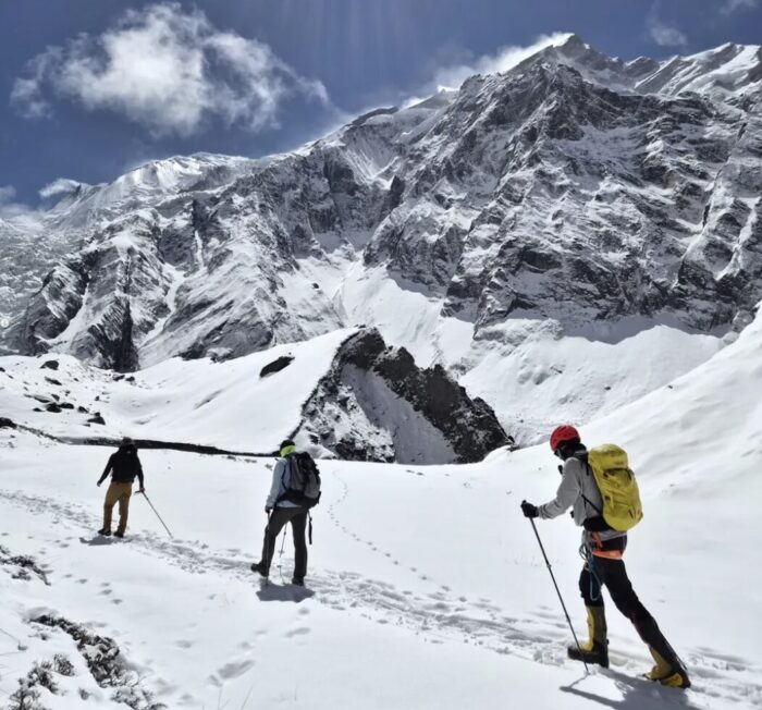 Three climbers roped up head up a trail in the snow with Annapurna in background.