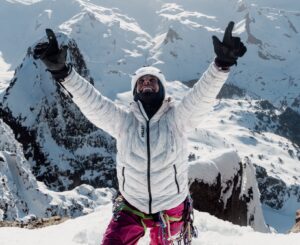 Climber Charles Dubouloz raises his arms in triumph on a snowy summit.