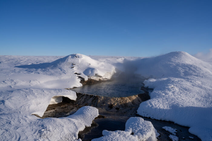 A steaming hot spring surrounded by snow