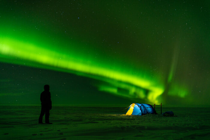 Stephane Weissbaum stands next to a tent under strong northern lights on Vatnajokull