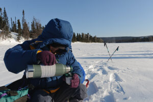 arctic traveler sitting on sled pouring drink