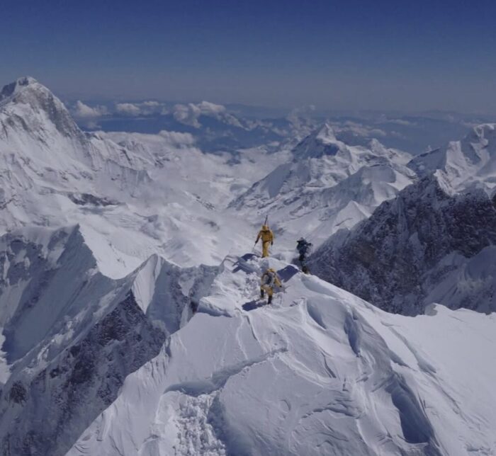 A small group of climbers on the summit of Everest, surrounded by mountains.