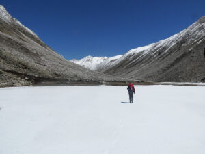 A lonel trekker on a flat ice surface heading to far away mountains.