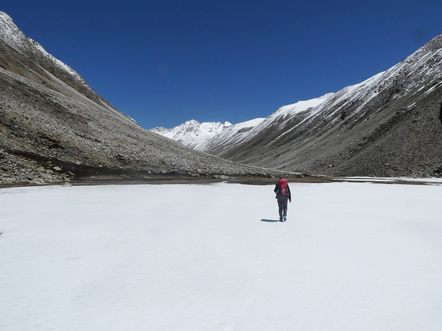 A lonel trekker on a flat ice surface heading to far away mountains.