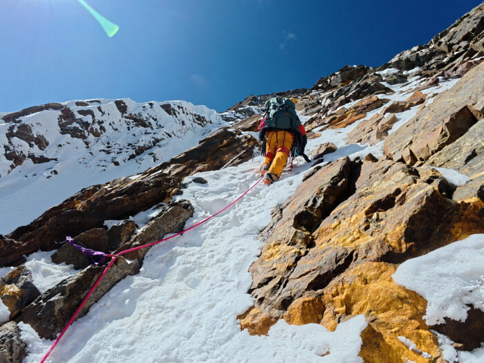 A climber on a steep scree slope covered with some snow. 