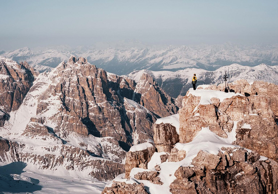 A climber on a dolomitic summit still covered in snow.