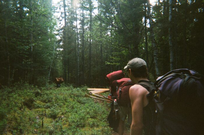A canoe carries a pack and paddles on a portage through dense woodland
