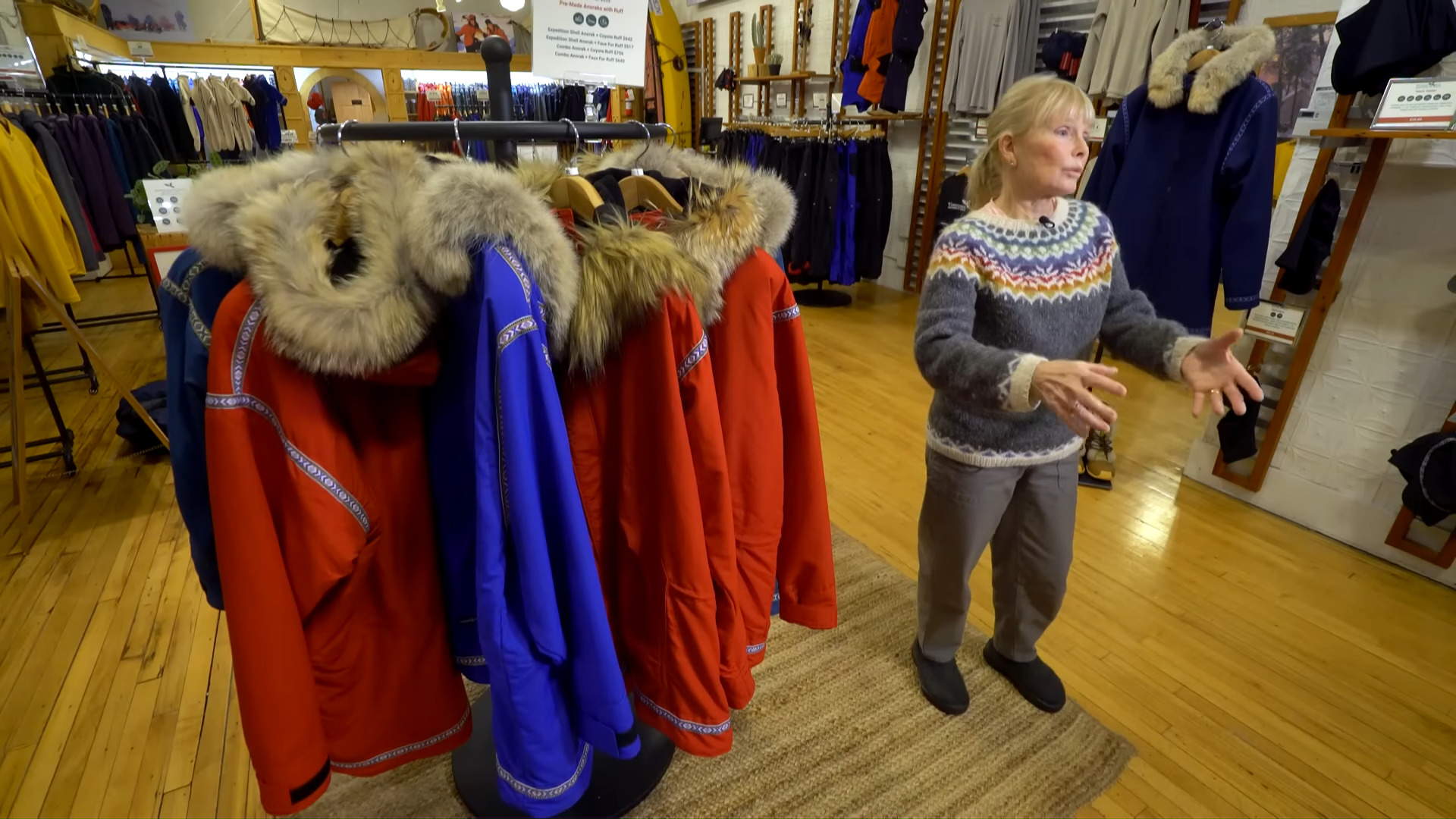 A woman in a workshop beside a rack of colorful anoraks.