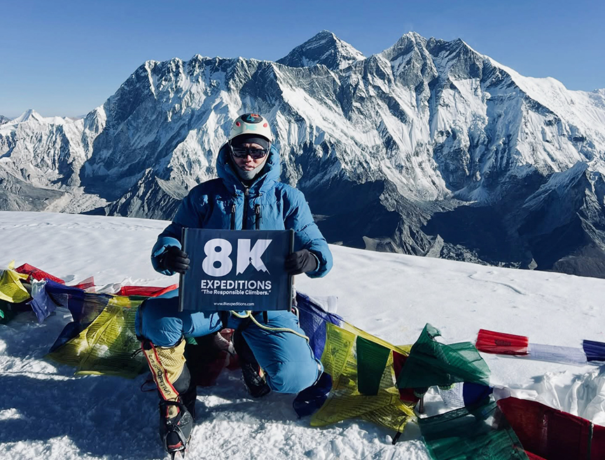 climber kneels in snow holding an 8K banner