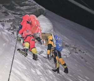 Two sherpa climbers fix ropes on a steep ramp as the snow falls in the night.