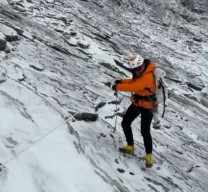 A climber clipped to afized rope descends on a slippery slope of scree covered with some fresh snow.