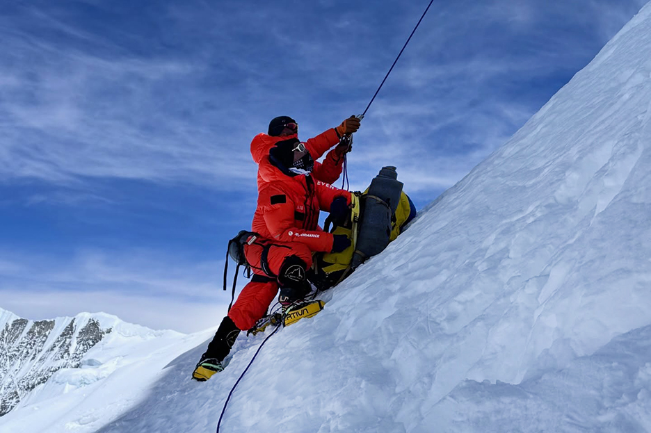 Climbers pull a rope on a steep snow slope.