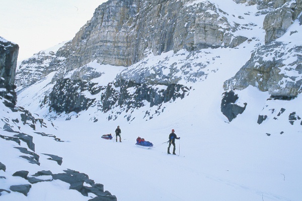 two sledders skiing past arctic cliffs