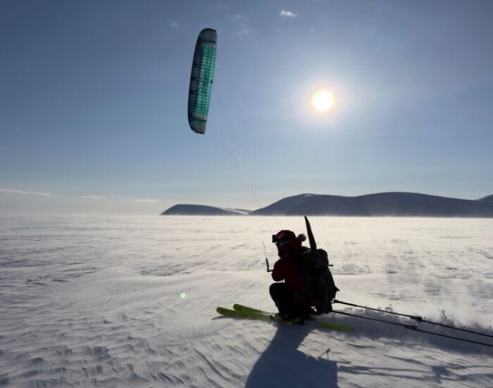 An adventurer snowkiting through sun drenched snow with the mountains of Svalbard in the background