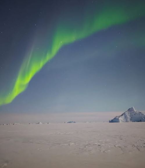 Northern lights shimmer over an iceberg