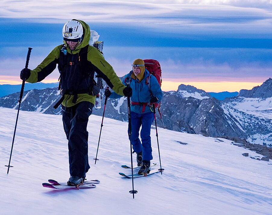 Two backcountry skiers on a hard snow slope at dawn.