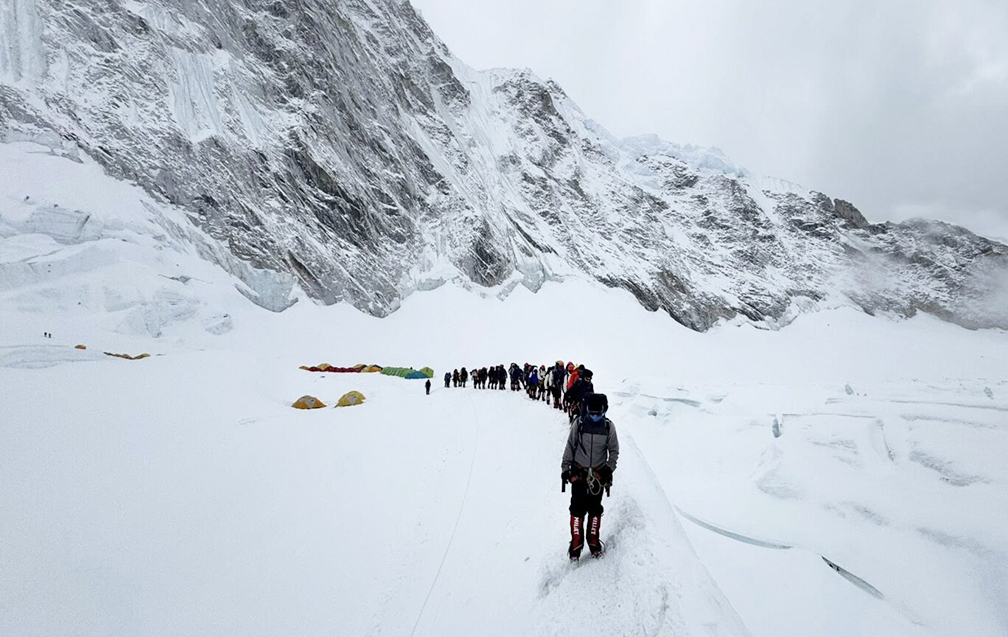 huge line of climbers walking through snow to camp