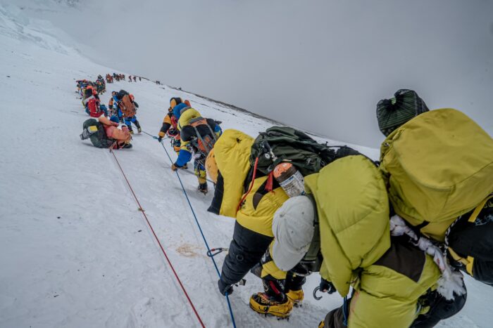 Climbers in line in a foggy day on Everest, clipped to a fixed rope.