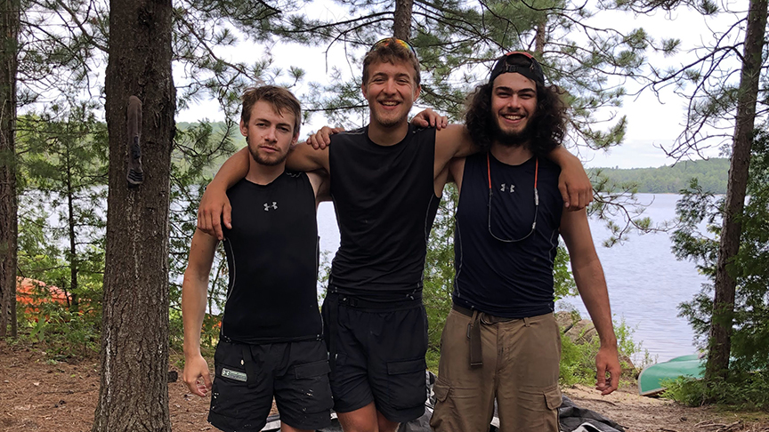 three young guys arm in arm in the woods