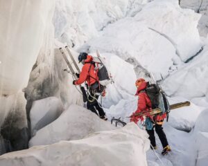 Two sherpa climbers among seracs with aluminium ladders.
