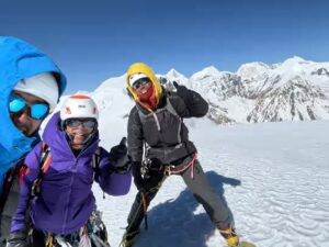 Three Japanese climbers smile from a flat, snowy summit.