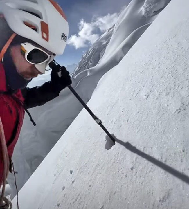 guy in helmet with ski pole on steep snow slope