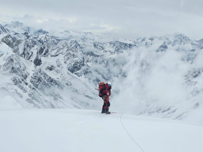 A climber on a snowy slope, mountains covered in fresh snow in background. 