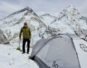 A climber by a small tent, Everest and Lhotse in background.