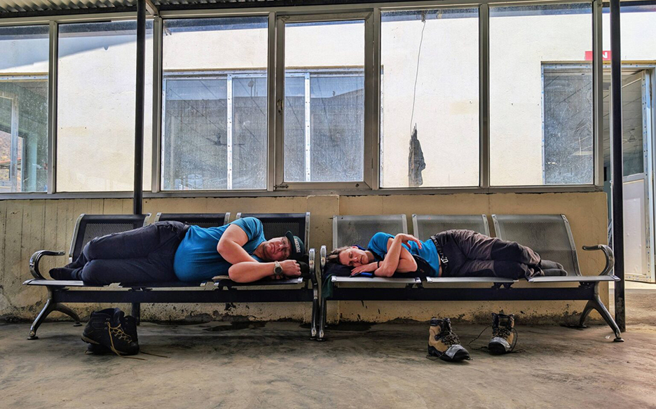 A man and a woman lay down on seats at a small airport loung in rural Nepal.