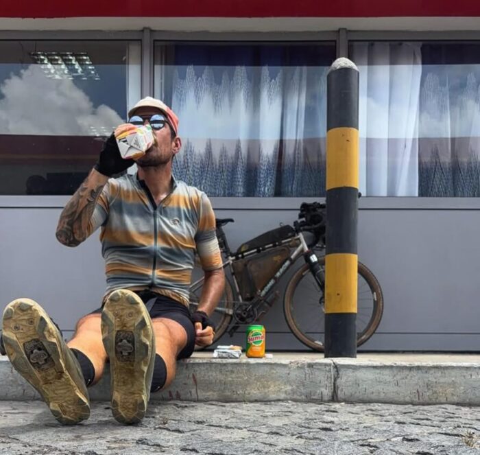 Swiss cyclist Adrien Liechti sits by a roadside drinking from a carton