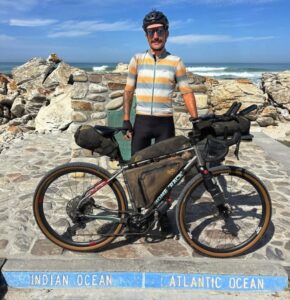 Swiss cyclist Adrien Liechti standing next to his bike at Cape Agulhas, the southernmost point in Africa