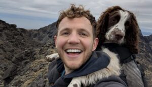 man in mountains with dog on shoulders.