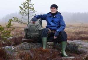 guy sitting on rock outdoors, with arm on backpack