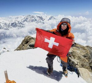 A woman on a snowy summit with a Swiss flag.