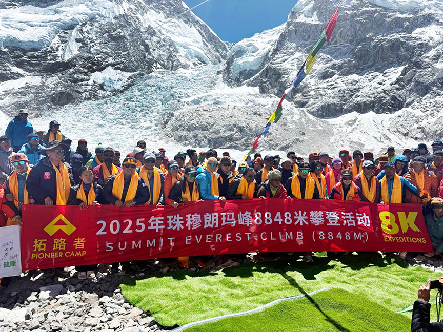 a huge group of climbers posing with a banner at Everest base Camp.