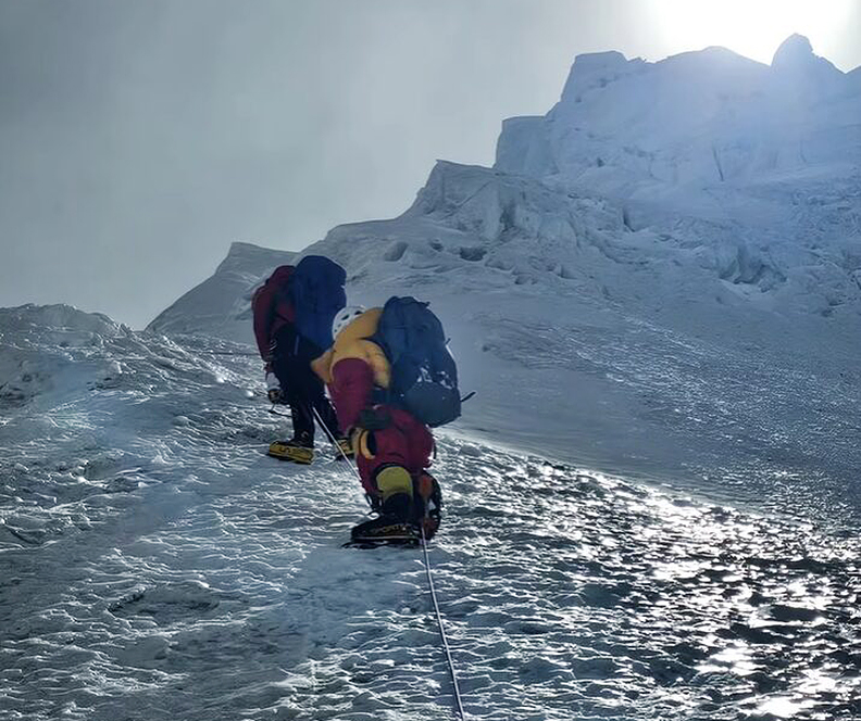 Two climbers clipped to a fixed rope on a steep ice ramp