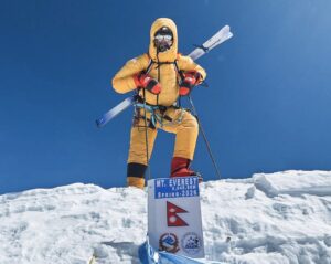 Bartek Ziemski stands on the summit of everest with skis strapped to his bckpack and an air-trimming mask.