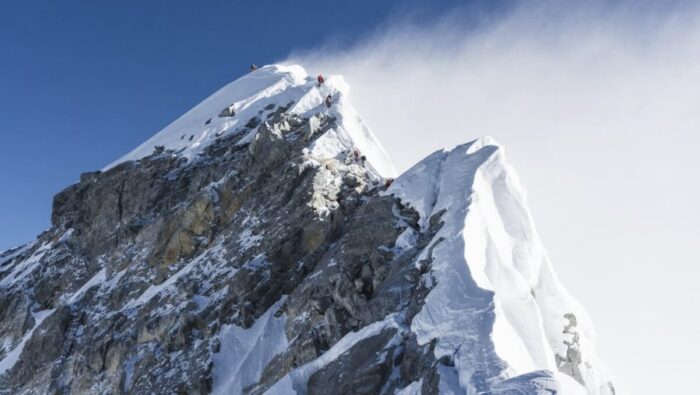 Everest's hillary step with a plume of high wind and some climbers on the snowy ridge. 