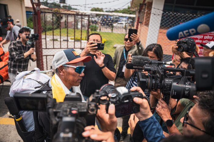 Kami Rita Sherpa witn cap and sunglasses, surrounded by cameras.