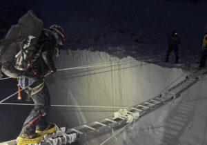 A climber in the night crossing a ladder on a crevasse.