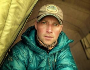 Close shot of climber saulius Damulevicius at the gate of a tent, with cap and dawn jacket.